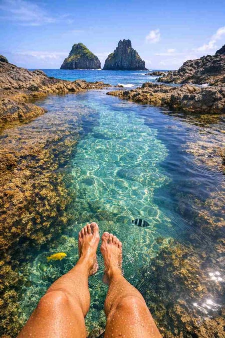 A relatable photo for the Baia dos Porcos guide showing feet in a clear natural pool, inviting viewers to imagine themselves there.