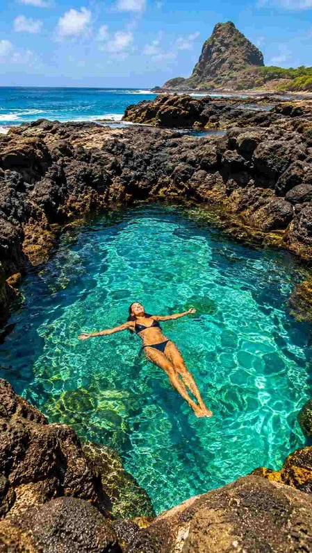 A person swimming in the turquoise natural pool at Praia do Cachorro, a highlight from our Fernando de Noronha travel guide.
