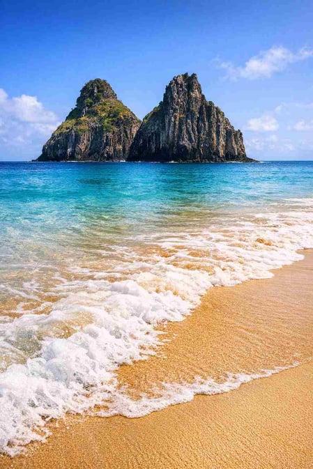 The iconic Morro Dois Irmãos rocks rising from the turquoise water at Cacimba do Padre Beach in Brazil.
