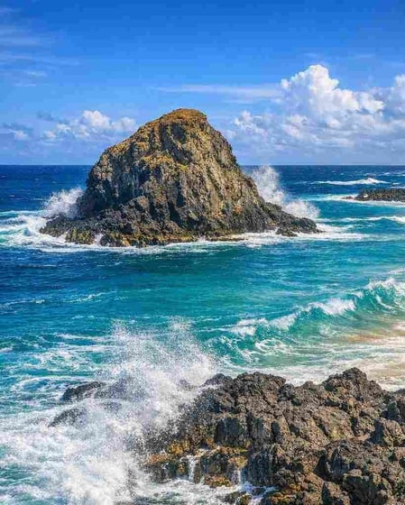The iconic lion-shaped rock at Praia do Leão in Fernando de Noronha, with powerful waves crashing on golden sand, as featured in our Leão Beach travel guide.