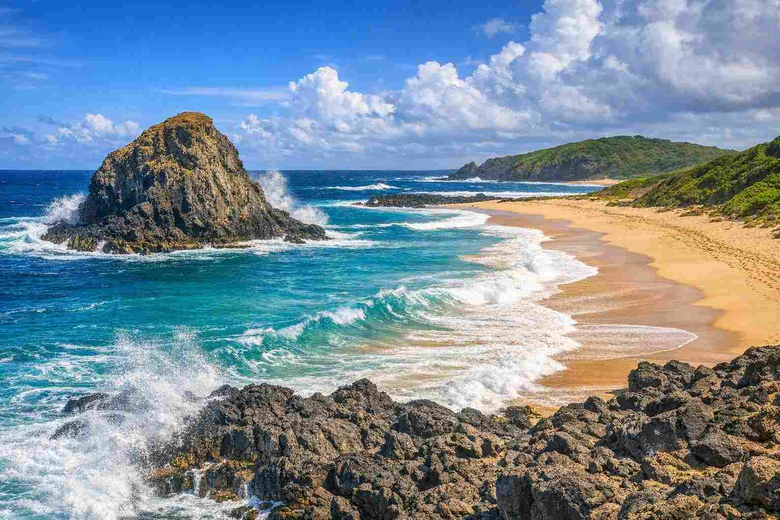The iconic lion-shaped rock at Praia do Leão in Fernando de Noronha, with powerful waves crashing on golden sand, as featured in our Leão Beach travel guide.