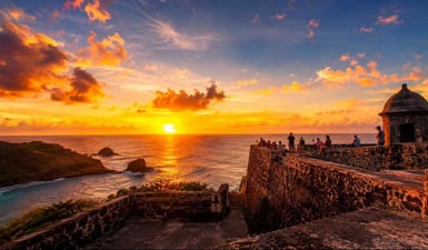 A panoramic sunset view from the historic ramparts in our Forte Noronha Guide, with the golden sun setting over the Atlantic Ocean.