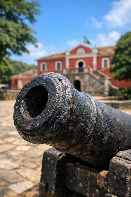 A close-up of a historic cannon in Fernando de Noronha, with the red São Miguel Palace in the background.