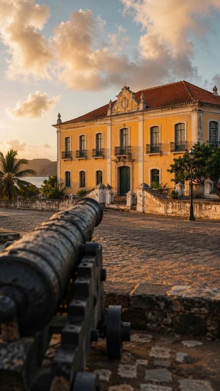 A historic cannon in the foreground with the São Miguel Palace in Fernando de Noronha in the background, bathed in warm light.