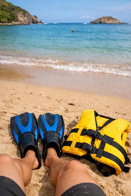 Una vista in prima persona delle pinne da snorkeling e di un giubbotto di salvataggio sulla sabbia, pronti per una visita alla spiaggia di Sueste.
