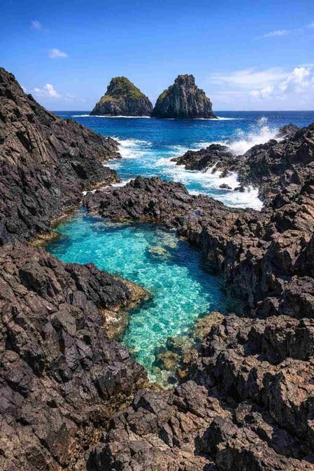 Una vista spettacolare tratta dalla guida di Baia dos Porcos, che mostra le rocce vulcaniche nere stagliarsi contro l'acqua turchese e il Morro Dois Irmãos.