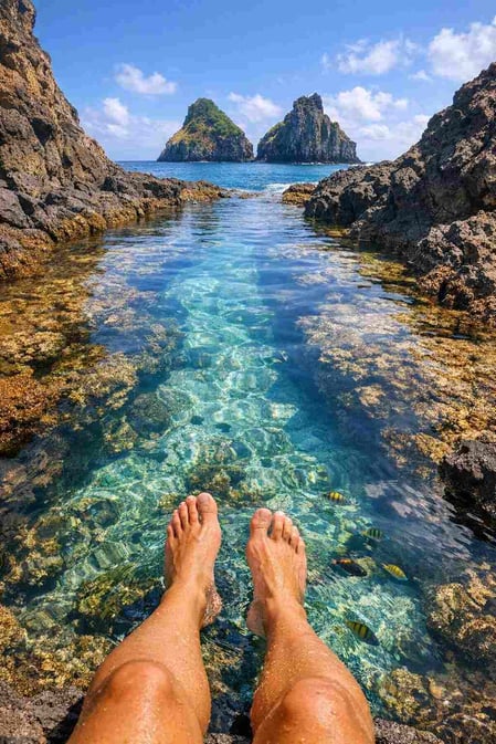 Una foto coinvolgente per la guida di Baia dos Porcos che ritrae dei piedi in una piscina naturale dalle acque cristalline, invitando chi la guarda a immaginarsi lì.