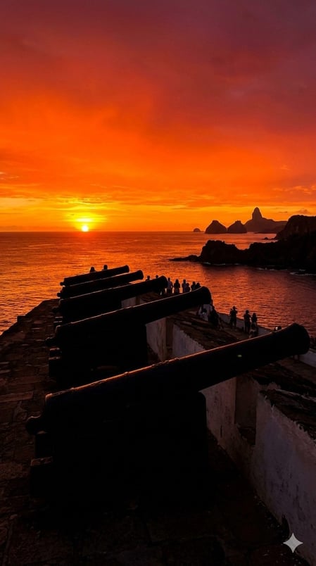 Cannoni storici stagliati contro un tramonto di un arancione infuocato nella nostra Guida al Forte Noronha, che presenta il miglior punto panoramico per ammirare il tramonto in Brasile.