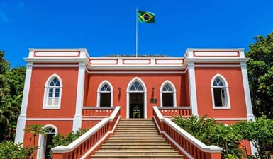 A fachada colonial em vermelho vivo do Palácio de São Miguel, em Fernando de Noronha, Brasil, sob um céu azul límpido com a bandeira brasileira hasteada.