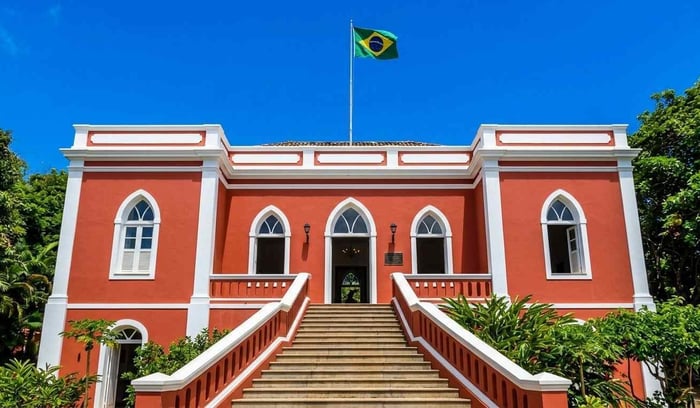 A fachada colonial em vermelho vivo do Palácio de São Miguel, em Fernando de Noronha, Brasil, sob um céu azul límpido com a bandeira brasileira hasteada.