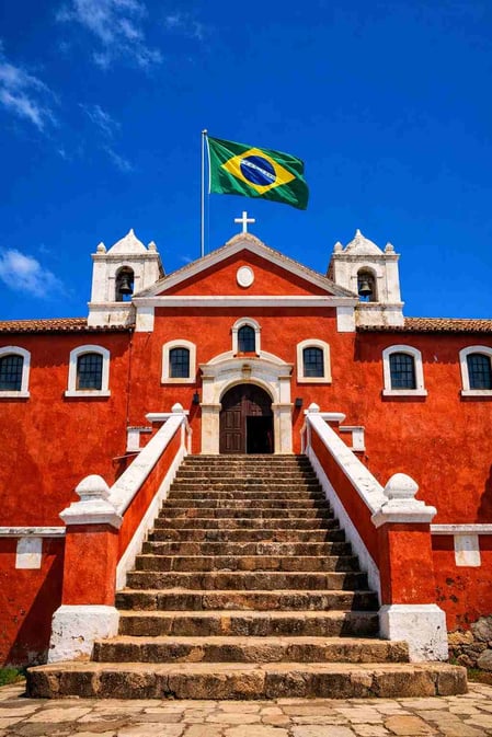 A imponente fachada vermelha do Palácio São Miguel, em Fernando de Noronha, Brasil, com uma legenda sobreposto perguntando: “Um palácio construído sobre as ruínas de uma prisão?”