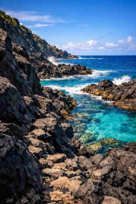 Uma vista espetacular do guia da Baía dos Porcos, mostrando rochas vulcânicas negras contra as águas azul-turquesa e o Morro Dois Irmãos.