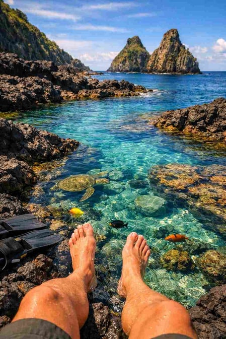Uma foto envolvente para o guia da Baía dos Porcos, mostrando pés em uma piscina natural de águas cristalinas, convidando os espectadores a se imaginarem ali.