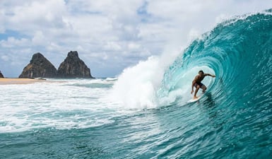 Um surfista desfrutando de um tubo poderoso na Praia da Cacimba do Padre, com as icônicas rochas do Morro Dois Irmãos ao fundo, no Brasil.