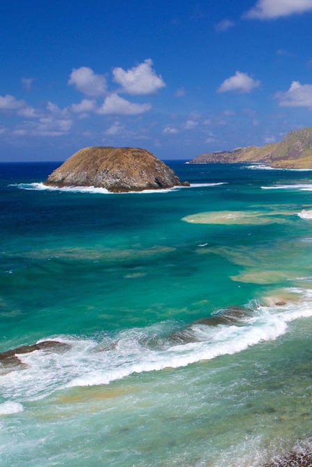 A icônica rocha em forma de leão na Praia do Leão, em Fernando de Noronha, com ondas poderosas quebrando na areia dourada, conforme apresentado em nosso guia de viagem da Praia do Leão.