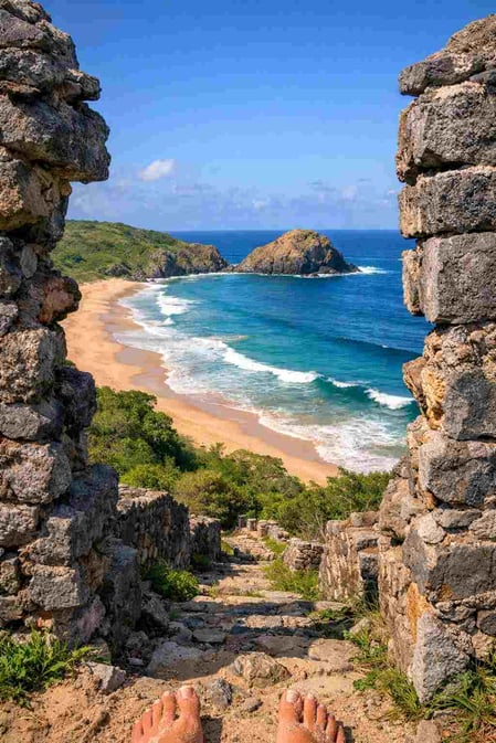 Vista panorâmica da costa emoldurada pelas ruínas da fortaleza histórica, um ponto imperdível para quem visita a Praia do Leão.